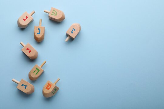 Wooden dreidels on light blue background, flat lay with space for text. Traditional Hanukkah game