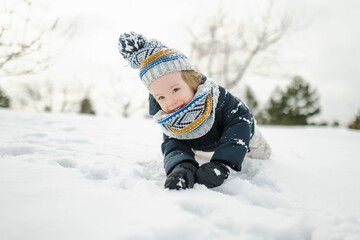 Fototapeta na wymiar Adorable toddler boy having fun in a backyard on snowy winter day. Cute child wearing warm clothes playing in a snow.