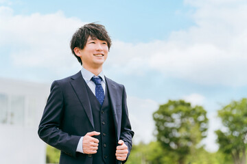 青空とオフィスの前に立つ若いアジア人ビジネスマン
