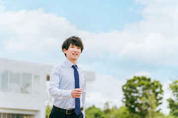 青空とオフィスの前に立つ若いアジア人ビジネスマン

