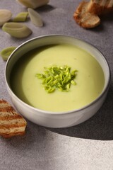 Bowl of delicious soup, cut leek and croutons on grey table