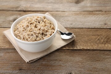 Tasty boiled oatmeal in bowl and spoon on wooden table, space for text
