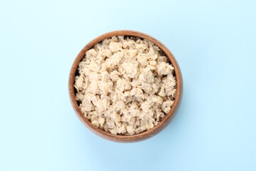 Tasty boiled oatmeal in bowl on light blue background, top view