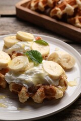 Delicious Belgian waffles with banana and whipped cream on table, closeup