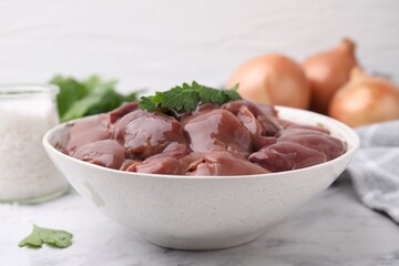 Bowl of raw chicken liver with parsley on white table, closeup