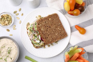 Tasty vegan sandwich with cucumber, onion, hummus and pumpkin seeds on light grey table, flat lay