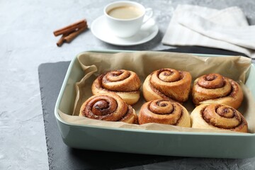 Baking dish with tasty cinnamon rolls on grey textured table, closeup