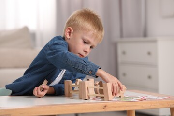 Cute little boy playing with set of wooden animals and fence at table indoors, space for text. Child's toy