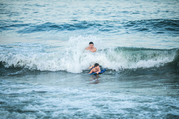Little surfer learn to ride on surfboard on sea wave. Father with son play in summer ocean, learning surfing. Little boy swim on  surf board