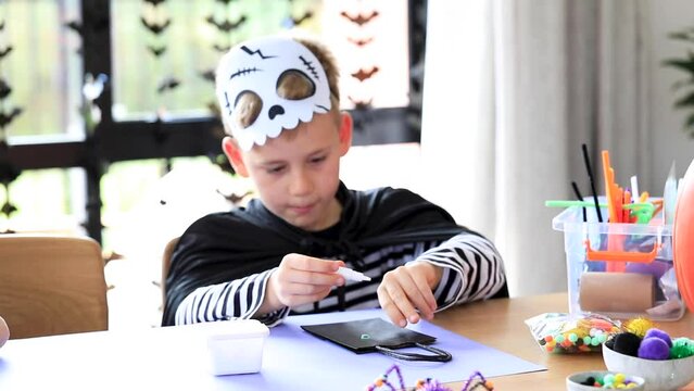 A cute boy in a skeleton costume makes crafts at the Halloween party.