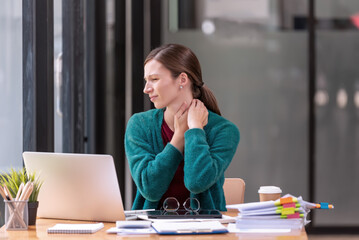 Young businesswoman office worker suffering from neck pain, massaging her neck at office table...