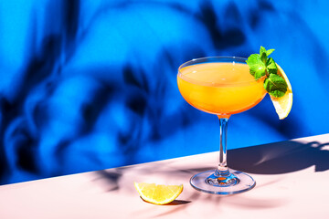 Paddington cocktail drink with rum, yellow liquor, grapefruit and lemon juice, marmalade and absinthe. Blue bright background, hard light and shadows