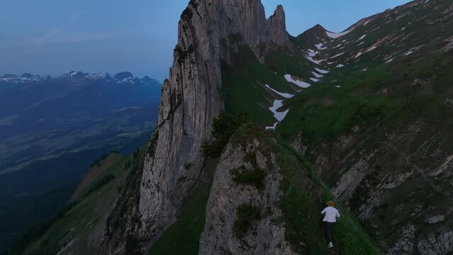 Drone footage of adult man walking on Saxer Lucke Viewpoint with Altmann Mountain in the background