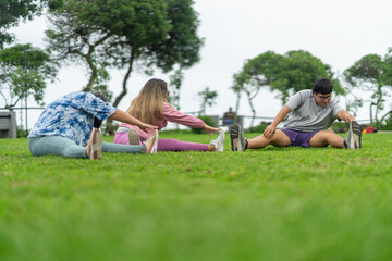 Overweight friends stretching sitting on the grass of a park