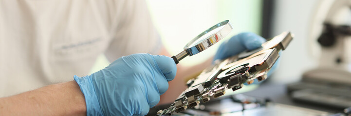 Obraz premium Man looks at printed circuit board through magnifier glass
