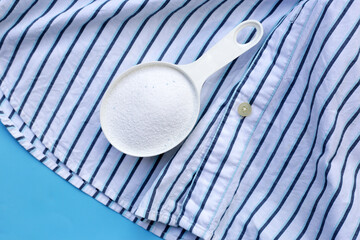 Detergent powder in measuring spoon on cloth before washing. Laundry concept.
