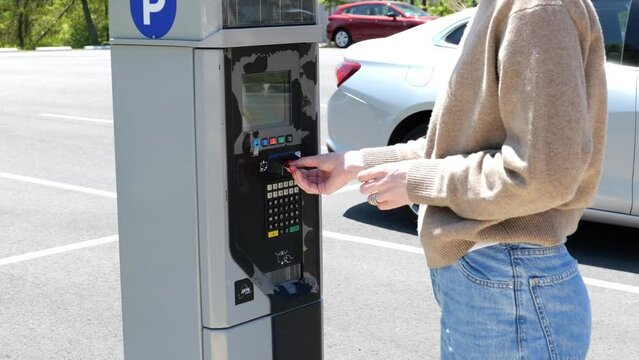 woman inserts card onto parking meeter, pays for parking