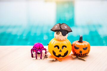 Cute wooden pirate ghost doll in Halloween pumpkin lantern and pink yarn spider on swimming pool edge, Happy halloween concept background idea
