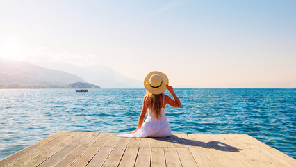 Woman in white dress and hat relaxing in front of the sea at sunset