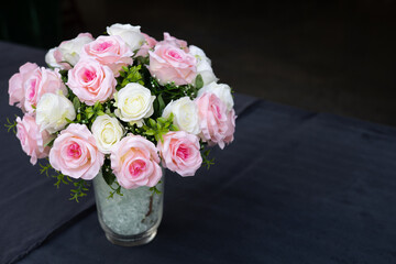 Vase of pink roses placed on a table covered with black fabric, spaced out copy space.