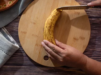 Fotobehang Concept of handling food. woman's hands cutting or peeling a banana on a cutting board, top view horizontal flat lay. © Victor