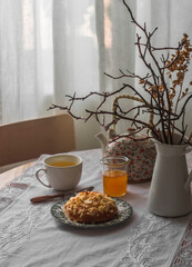 Tea party in a cosy living room. Cup of green tea, honey, a sweet bun on a round table