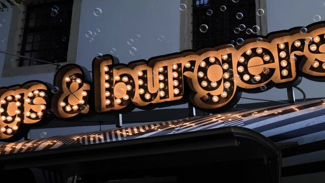 Illuminated Hot Dogs And Burgers Store Sign With Bubble Generator. low angle, pan right