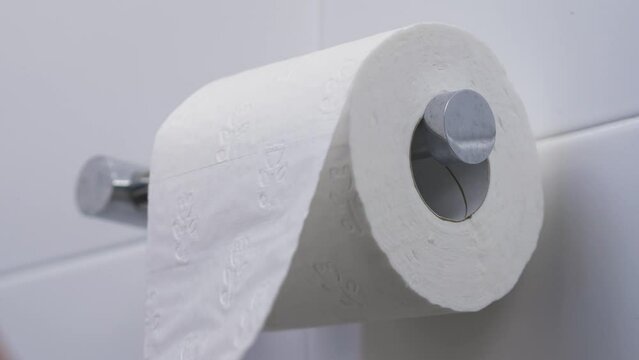 Close-up slow motion shot of pulling toilet roll tissue paper on toilet holder bathroom people personal hygiene loo 4K