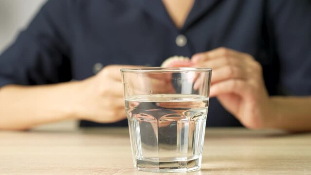 Elderly woman takes dentures out of her mouth and puts it in glass of water