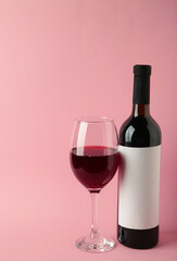 Wine bottle and wine glass on pink background. Vertical photo