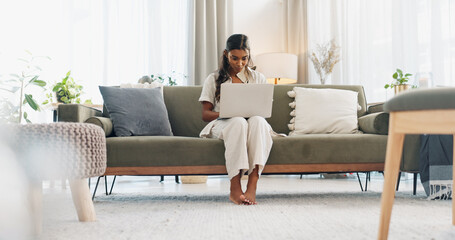 Woman, laptop and typing on sofa for communication, email or social media scroll in living room of home. Indian, girl and pc for freelance web search, streaming or technology with internet in lounge - obrazy, fototapety, plakaty