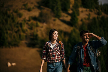 A diverse couple joyfully hiking on a sunny day, with backpacks in tow