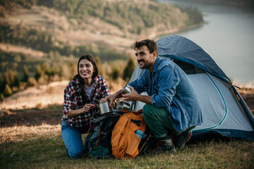 A diverse couple happily preparing for a cooking on a camp stove on a sunny camping day - Powered by Adobe