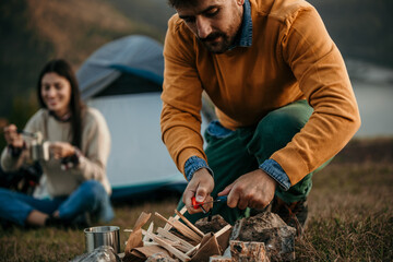 A diverse couple enjoys a serene tent camping experience by a glistening lake as the man skillfully...