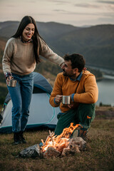 An affectionate couple embraces by the campfire as the sun sets over the serene lake in the...