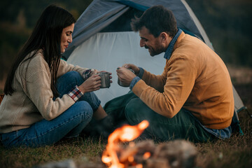 Sweet moments of a loving couple bonding by the campfire with a stunning lake scene - obrazy, fototapety, plakaty