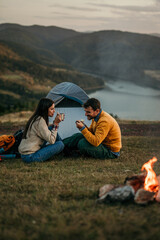 A couple cuddling on a hilltop campsite, with a lake in the background