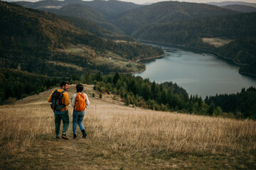 Fototapeta na wymiar Young couple trekking with backpacks, gazing at a lake far away
