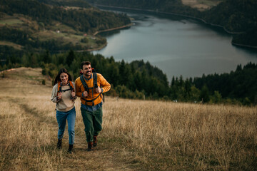 Happy couple hiking with backpacks on a hill, enjoying the view of a distant lake