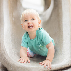 Fototapeta premium Child playing on outdoor playground. Toddler plays on school or kindergarten yard. Active kid on stone sculpured slide. Healthy summer activity for children. Little boy climbing outdoors