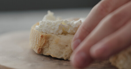 spread cream cheese on fresh baguette slice on olive board closeup