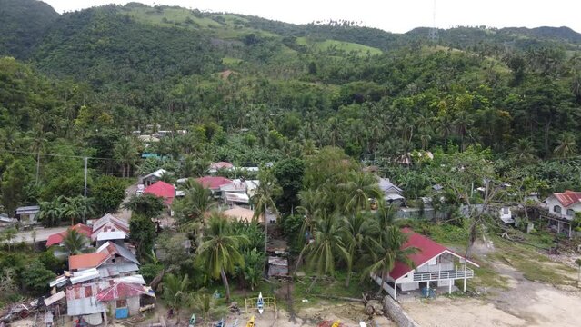 Filipino villager seaside houses and coastline road traffic at lush green overgrown foothill on Cebu island. Aerial dolly in