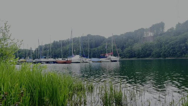Some sailing boats on a jetty on the lake of the aggertalsperre with reeds in the forest in the background