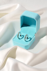 White gold earrings in blue jewelry box on silk background