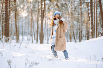 Fototapeta na wymiar Smiling woman in a winter snow-covered park walks and plays with snow on a beautiful sunny day. Young fashionable woman in the winter forest. Walking concept, weekend.