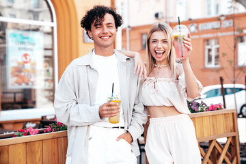 Young smiling beautiful woman and her handsome boyfriend in casual summer clothes. Happy cheerful family. Female having fun. Couple posing in street. Holding and drinking cocktail drink in plastic cup