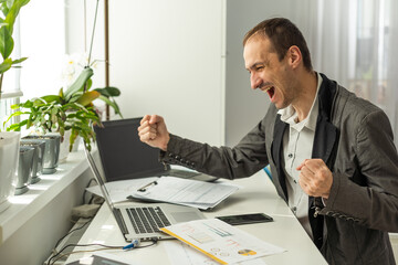 Naklejka premium Victory concept. Successful cheerful lucky caucasian bearded businessman, ceo company, manager, sits at work desk in the office, gesturing with fists