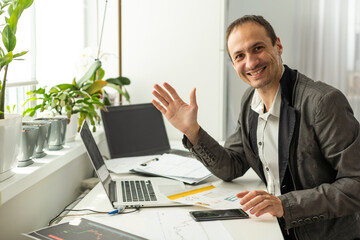 Naklejka premium Positive caucasian professional business man, mentor, waving hand and looking at webcam during video conference, listens lecture, leading webinar, record online training, smiling friendly