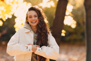Smiling young woman cold autumn portrait in the forest with the yellow leaves at sunset - 664796751
