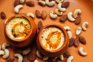 Kulfi ice cream in two clay pots on a solid orange background with cashews and almonds. Kulfi is a popular traditional Indian dessert made of milk with spices and nuts - obrazy, fototapety, plakaty
